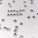 White Scrabble tiles forming the phrase 'social media' on a scattered background. Des tuiles Scrabble blanches formant la phrase « réseaux sociaux » sur un fond dispersé.