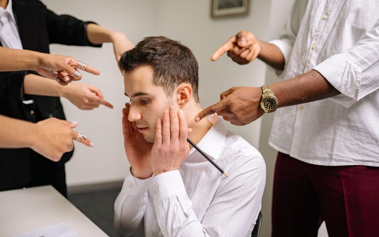 Homme stressé au bureau entouré de doigts accusateurs